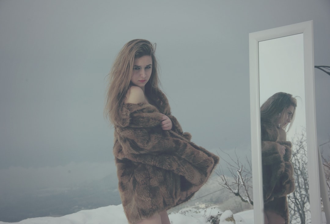 woman in brown coat facing mirror